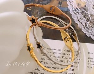 Close-up of star-pendant bangles in rose gold, gold and silver on a ceramic vase