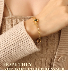 Macro shot of gold star bracelet with black enamel and zircons on a model's wrist