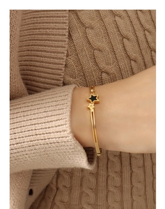 Detail of star-shaped spring clasp bracelet in gold finish worn over a beige sweater