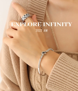 Detail of silver star bracelet and checkerboard enamel ring worn on a beige knit sleeve