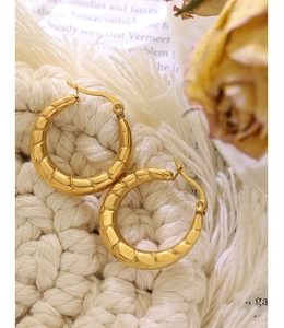 Vista macro degli orecchini a U placcati oro 18K con una trama trapuntata a croissant