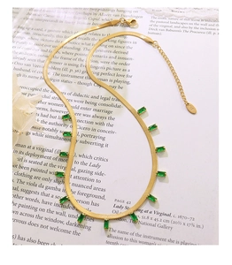 Détail d'un collier chaîne serpent dorée avec pendentifs en zircon vert sur un livre