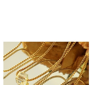 Détail d'un collier chaîne box dorée avec un pendentif cube en verre sur un miroir