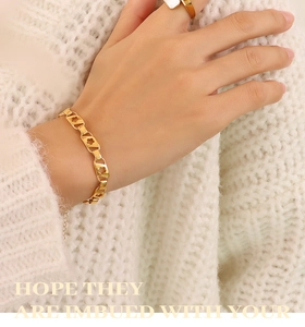 Gros plan d'un bracelet fleuri doré et d'une bague large sur un pull en maille