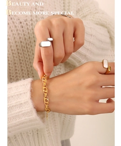 Gros plan d'un bracelet fleuri doré et de bagues géométriques sur un pull en maille
