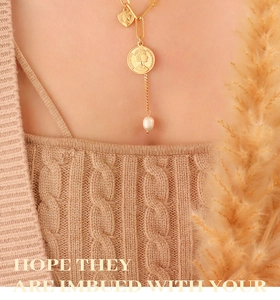 Gros plan du collier double couche avec pièce dorée, cœur et perle sur pull en maille