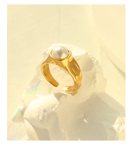 Macro detail of gold-plated open ring with white pearl on minimalist stone background