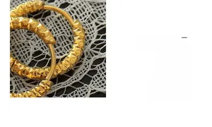 Gros plan sur des créoles dorées à l'or 18 carats avec texture martelée sur dentelle blanche