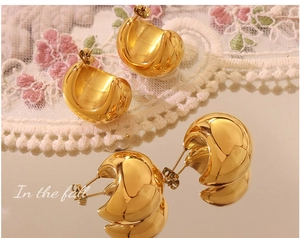 Detail of chunky gold C-shaped hoop earrings with polished mirror finish on lace
