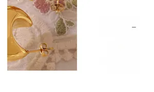 Close-up of minimalist 18K gold plated hollow C-shape earrings on white lace fabric