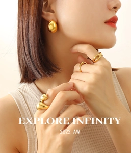 Close-up of golden hollow C-shaped earrings and rings set on a model with liquid metal style