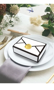 Detail of vintage envelope gift box with black borders and golden wax seal on dining plate