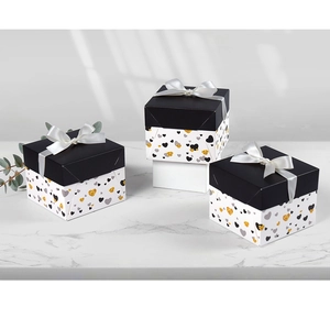 Three square gift boxes with black lids and gold heart patterns on marble surface