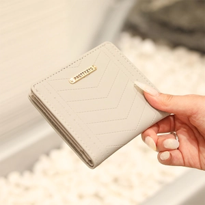Detail of cream short folding wallet featuring V-shaped stitching and golden logo plate