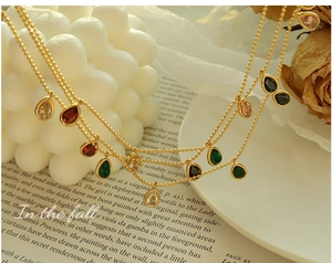 Detail of gold beaded necklace with colorful teardrop zircon charms on white props