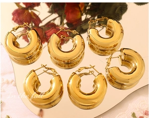 Three pairs of chunky gold hoop earrings displayed on a mirror with floral decor