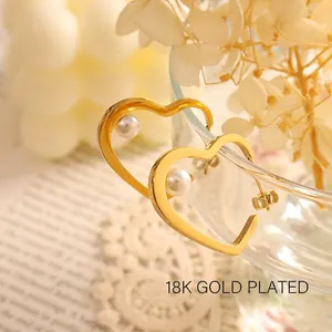 Polished heart-shaped 18K gold plated earrings with pearls on a glass rim