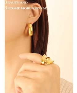Close-up of gold geometric earrings and wavy band ring set on model in warm lighting