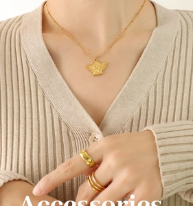 Close-up of golden angel pendant necklace in 18k gold plating on a beige knit cardigan