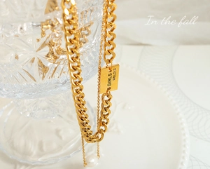 Detail of gold Cuban link chain with 'GIRLS WELOVE' engraved tag and white pearl pendant
