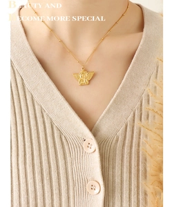 Close-up of golden angel pendant necklace on model with bead chain detail and beige knit