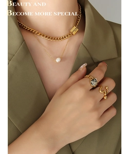 Detail of layered gold-plated necklaces with pearl pendant and chain rings on a model