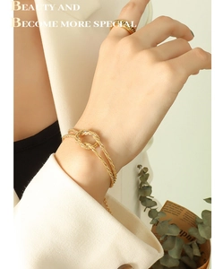 Detail of gold knot bracelet and chain ring worn with a professional white blazer
