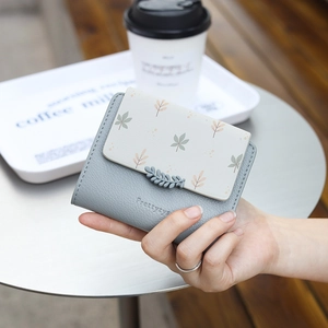 Close-up of a grey leaf-print faux leather wallet held by hand in a bright cafe setting
