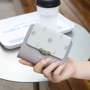 Short PU leather wallet with leaf print and buckle being held in a coffee shop setting