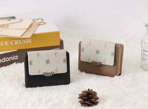 Detail of PU leather floral wallets in black and brown on a soft white plush rug
