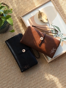 Detail of long leather wallets with leaf embroidery and wristlets on a straw mat