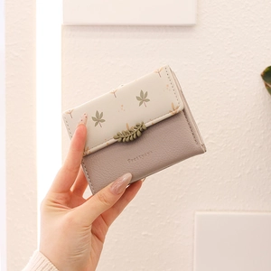 Detailed close-up of a lilac and floral folding wallet with leaf buckle held by a hand