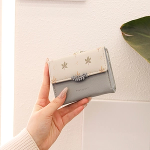 Detail of floral fold-over wallet with brown leaf charm and brand logo embossing