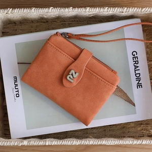 Close-up of orange matte PU leather wallet with ZN metal logo and wrist strap on book