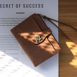 Detailed macro view of a brown suede mini wallet with a gold metal PZ logo and wrist strap