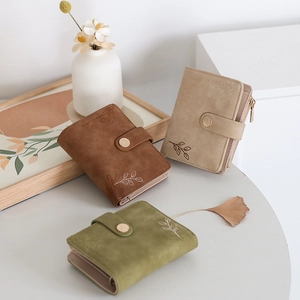 Detailed view of three suede wallets in brown beige and green with leaf embossing