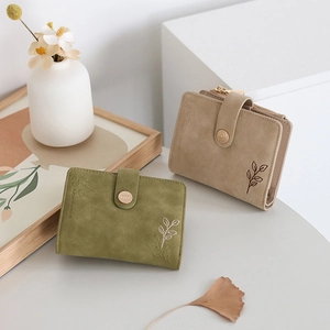 Close-up of olive green and khaki faux suede wallets with delicate leaf embroidery details