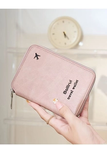 Pink faux leather travel wallet with airplane icon and silver zipper held by hand