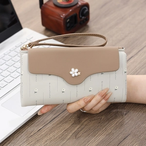 Detail of a bi-color long wallet featuring a floral metal clasp and hand strap on a desk