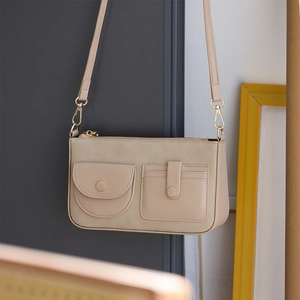Dettaglio borsa beige in tessuto Oxford con tasche frontali e ganci in metallo oro