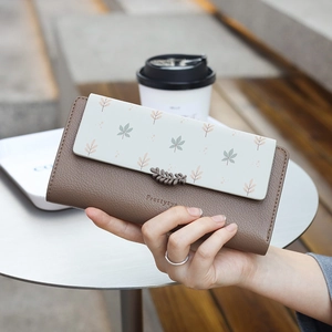 Gros plan du portefeuille long à motif de feuilles tenu à une table de café en cuir chic