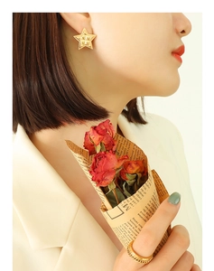 Close-up of 18k gold-plated star stud earrings and chunky chain ring on a female model