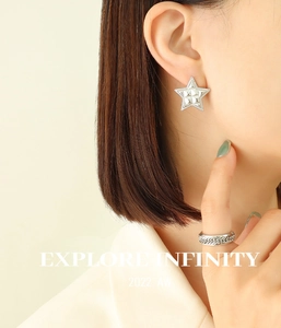 Macro shot of silver star stud earring and woven textured open ring on model