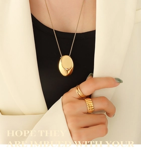 Détail d'un collier à pendentif ovale doré et bagues texturées avec un blazer