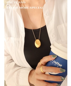 Détail du pendentif ovale et des bagues dorées portés avec une tenue élégante et chic