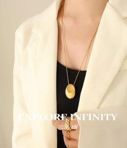 Détail du collier pendentif ovale doré et des bagues avec logo sur blazer blanc