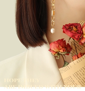 Detail of elegant gold link earrings with a hanging pearl on a model with red roses