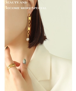 Close-up of geometric link earrings with freshwater pearls and a textured gold ring