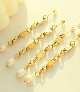 Detailed view of long gold titanium earrings featuring chain links and irregular pearls