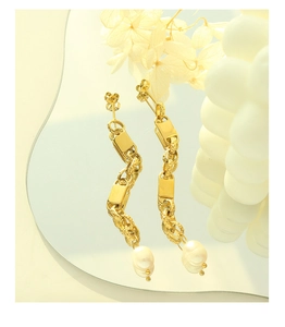 Close-up of golden geometric chain earrings with natural white baroque pearls on mirror